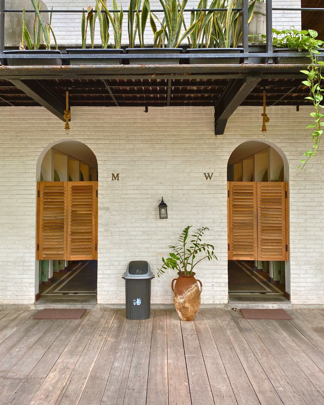 A building facade with two wooden shutters, a trash bin, and a potted plant.