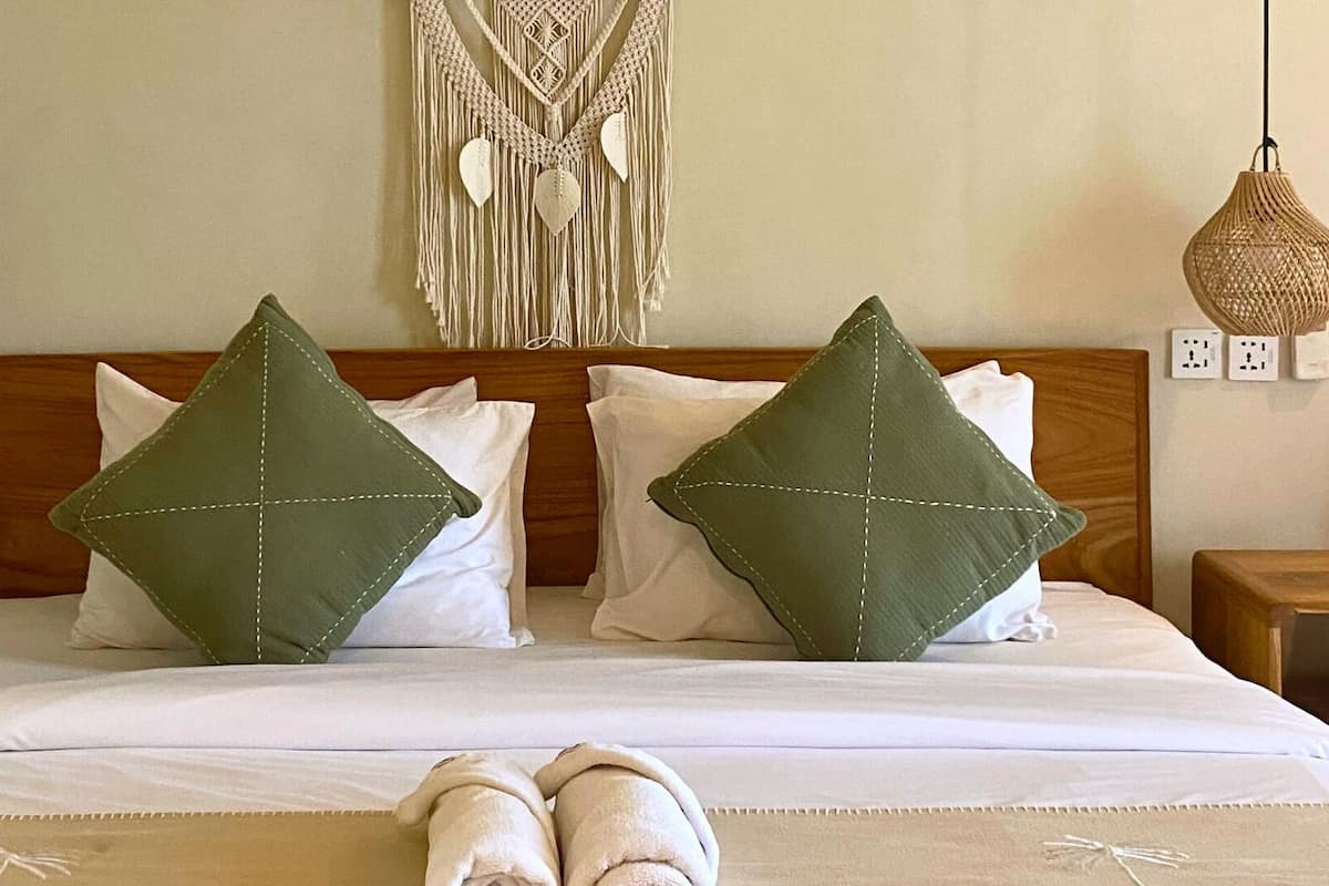 A bed with two green pillows, a macrame wall hanging, and two wicker lamps.