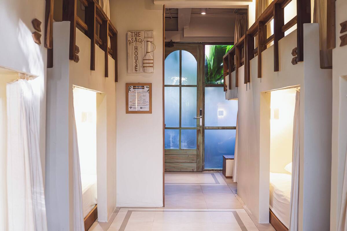 A hotel corridor with wooden beds, a tiled floor, and a view through a glass door.
