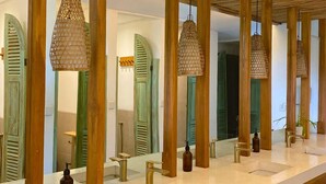 A bathroom with wooden beams, multiple sinks, and hanging pendant lights. - White Penny Hostel (Keroboken Kelod)