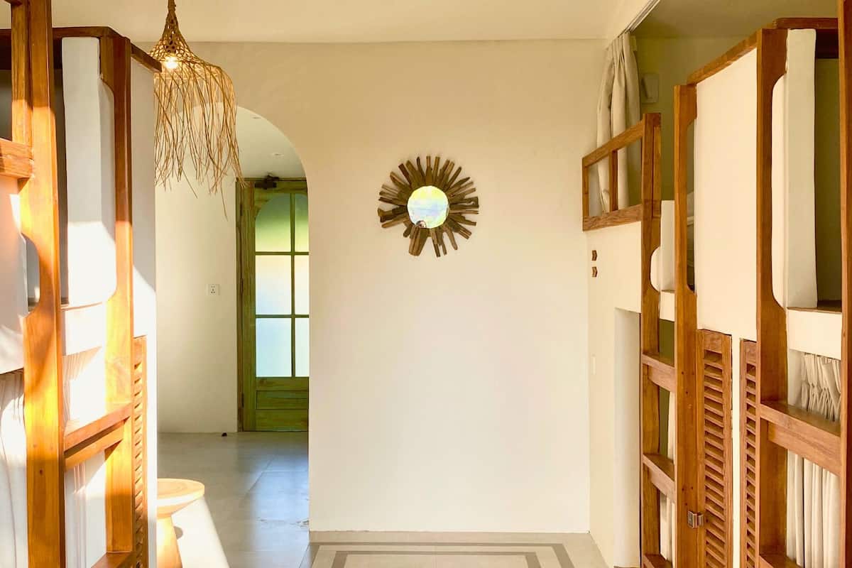 A hallway with a wooden door frame, a hanging light fixture, and a wall-mounted sunburst mirror.