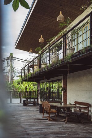 A wooden deck with a table and chairs, a bench, and potted plants. - White Penny Hostel (Seminyak)