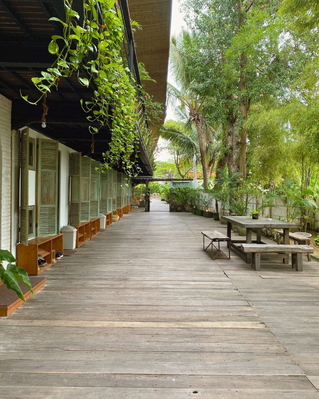 A covered wooden deck with benches and tables, surrounded by lush greenery and trees.