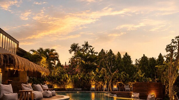 A pool with lounge chairs and a building with a thatched roof. - White Penny Hostel (Keroboken Kelod)