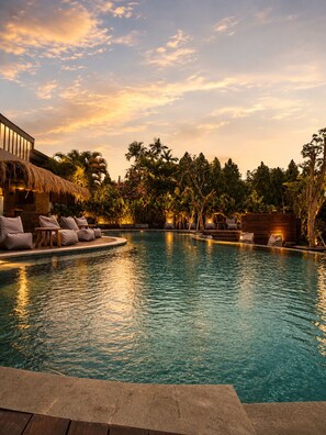 A pool with lounge chairs and a building with a thatched roof. - White Penny Hostel (Keroboken Kelod)