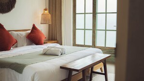 A bedroom with a bed, pillows, a bench, a lamp, and a window. - White Penny Hostel (Keroboken Kelod)