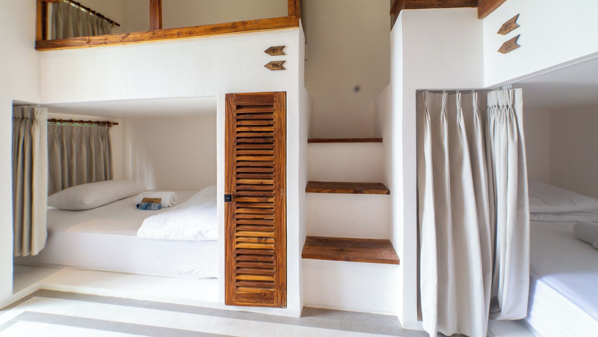 A room with two bunk beds, wooden shutters, a staircase, and curtains.