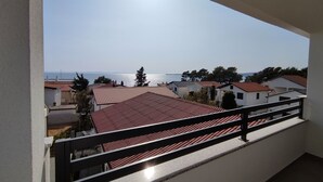 A balcony with a view of a coastal area, featuring houses with red-tiled roofs and a clear sky. - Bloom Apartments & Lounge Bar (Vir)