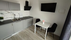 A compact kitchen with a sink, cabinets, and a dining area with a table and chairs. - Bloom Apartments & Lounge Bar (Vir)