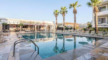 A pool area with lounge chairs, palm trees, and a clear sky.