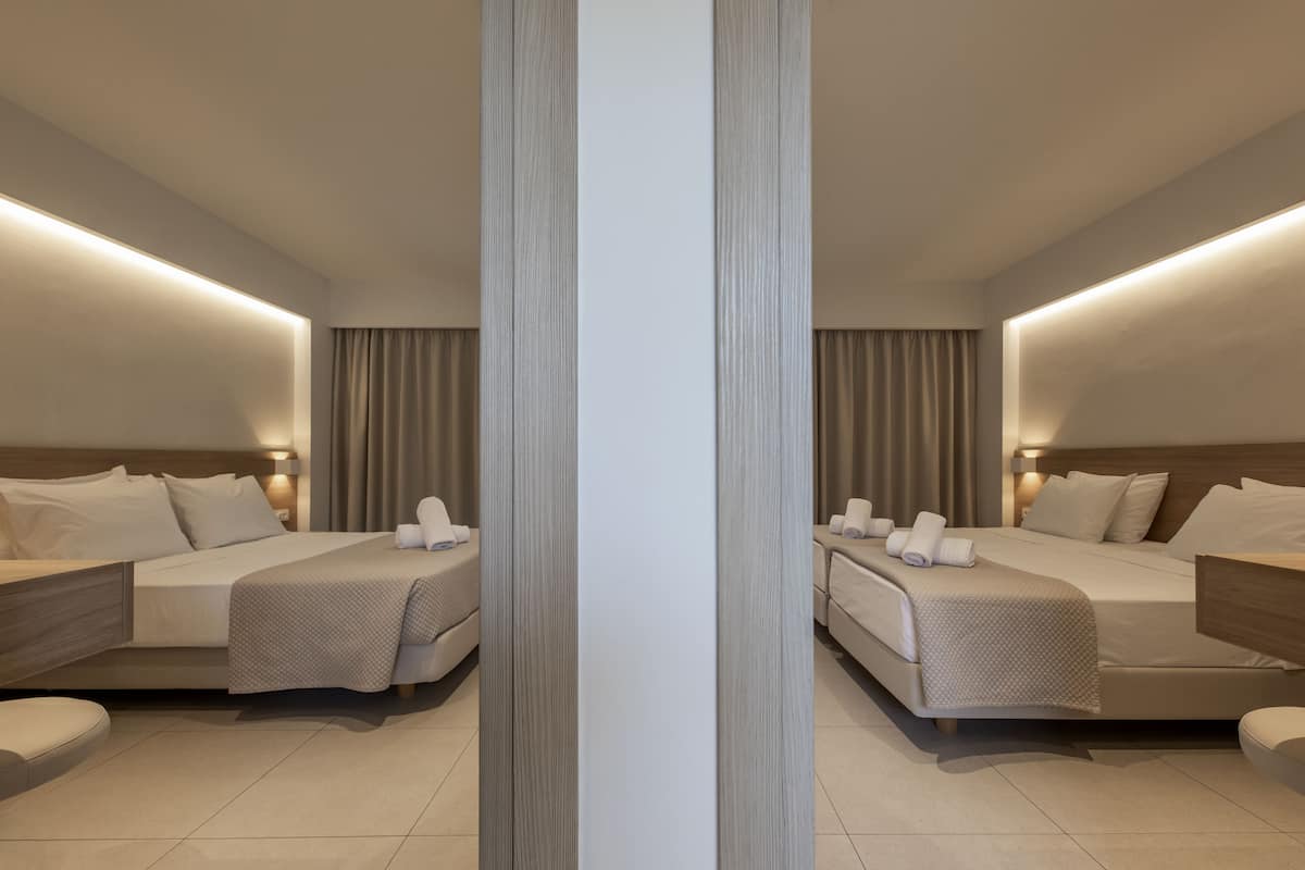 A mirrored hotel room with two beds, a nightstand, and a chair.