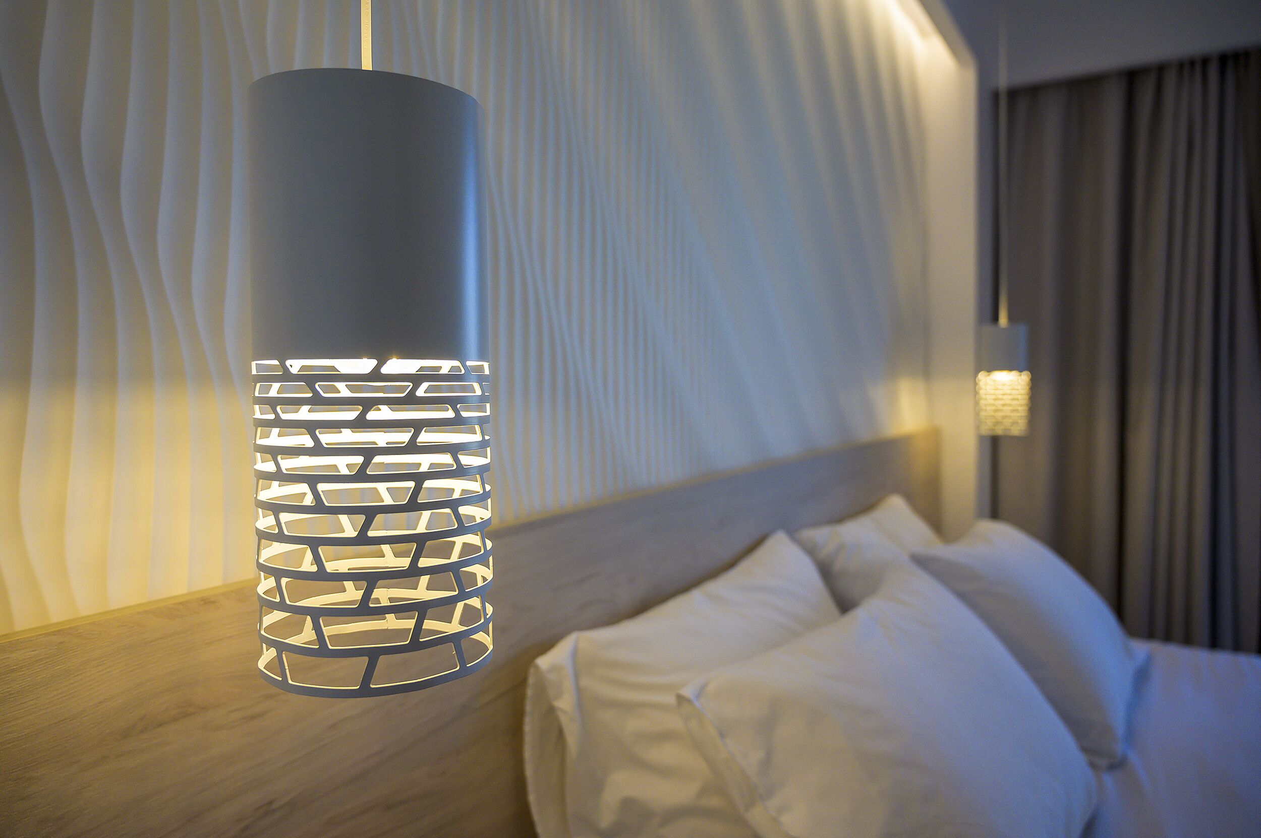 A modern hotel room with a bed, a decorative hanging light fixture, and a textured wall.