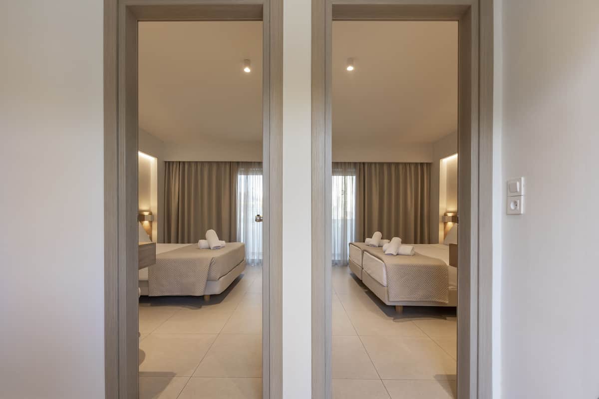 A mirrored view of a hotel room with two beds, a large window with curtains, and a door with a handle.
