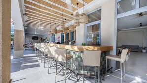 Un área de bar moderna con una barra alargada, varios taburetes y lámparas colgantes de mimbre.