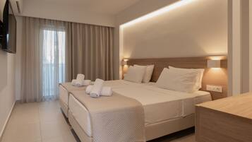 Habitación de hotel con una cama grande, una mesita de noche, un televisor montado en la pared y un ventanal con cortinas.