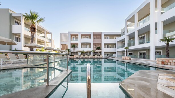 Un hotel moderno con piscina central, varios balcones y tumbonas.
