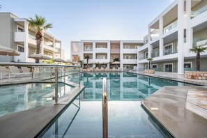 A modern hotel with a central swimming pool, multiple balconies, and sun loungers.