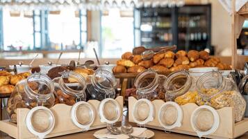 Ein Frühstücksbuffet mit verschiedenen Backwaren und Speisen, die in Gläsern und Körben angerichtet sind.