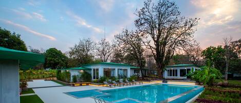 Uma área de piscina moderna com uma grande piscina retangular, espreguiçadeiras e um jardim bem cuidado.