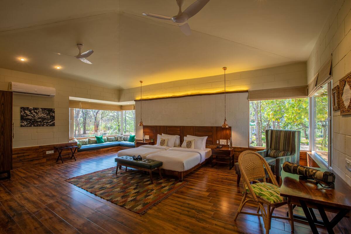 A spacious bedroom with a large bed, a sitting area with a bench, a dining table, and a view of the outdoors.