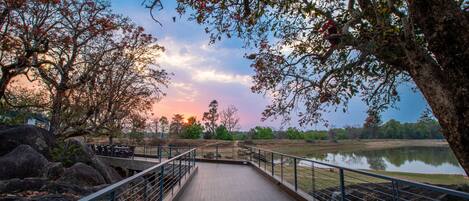 A wooden deck with metal railings overlooking a calm body of water and trees.