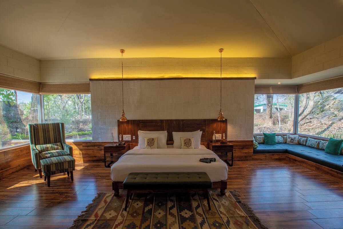 A spacious bedroom with a large bed, a bench, a chair, and a view of the outdoors.