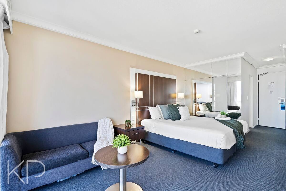 A hotel room with a large bed, a sofa, a small round table, and a mirror.