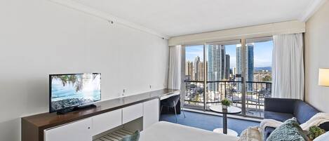 A modern hotel room with a balcony, a TV, a dining area, and a city view.