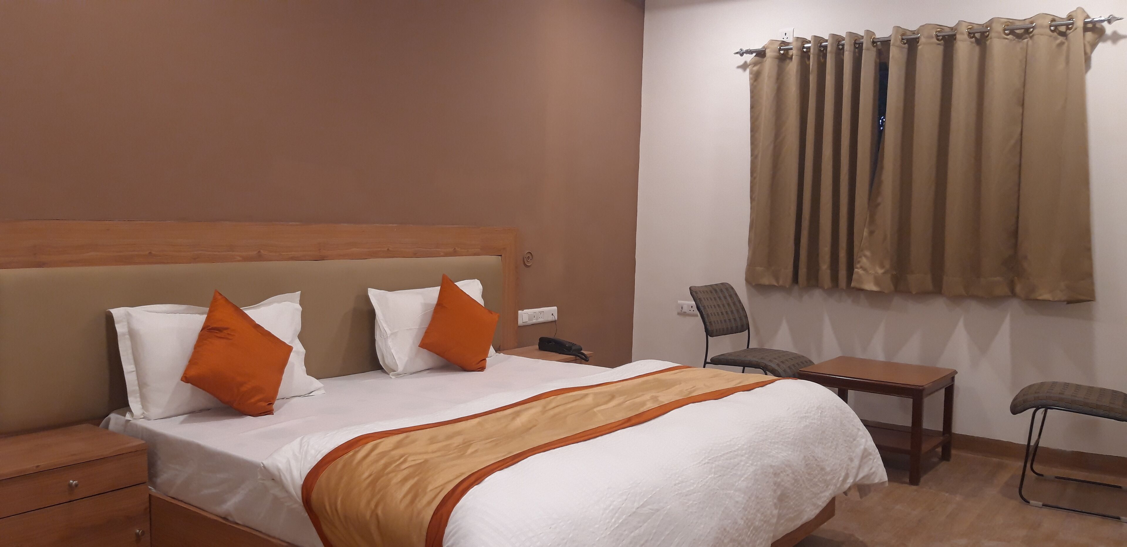 Ein Hotelzimmer mit einem Bett, zwei Stühlen, einem kleinen Tisch und einem Fenster mit Vorhängen.