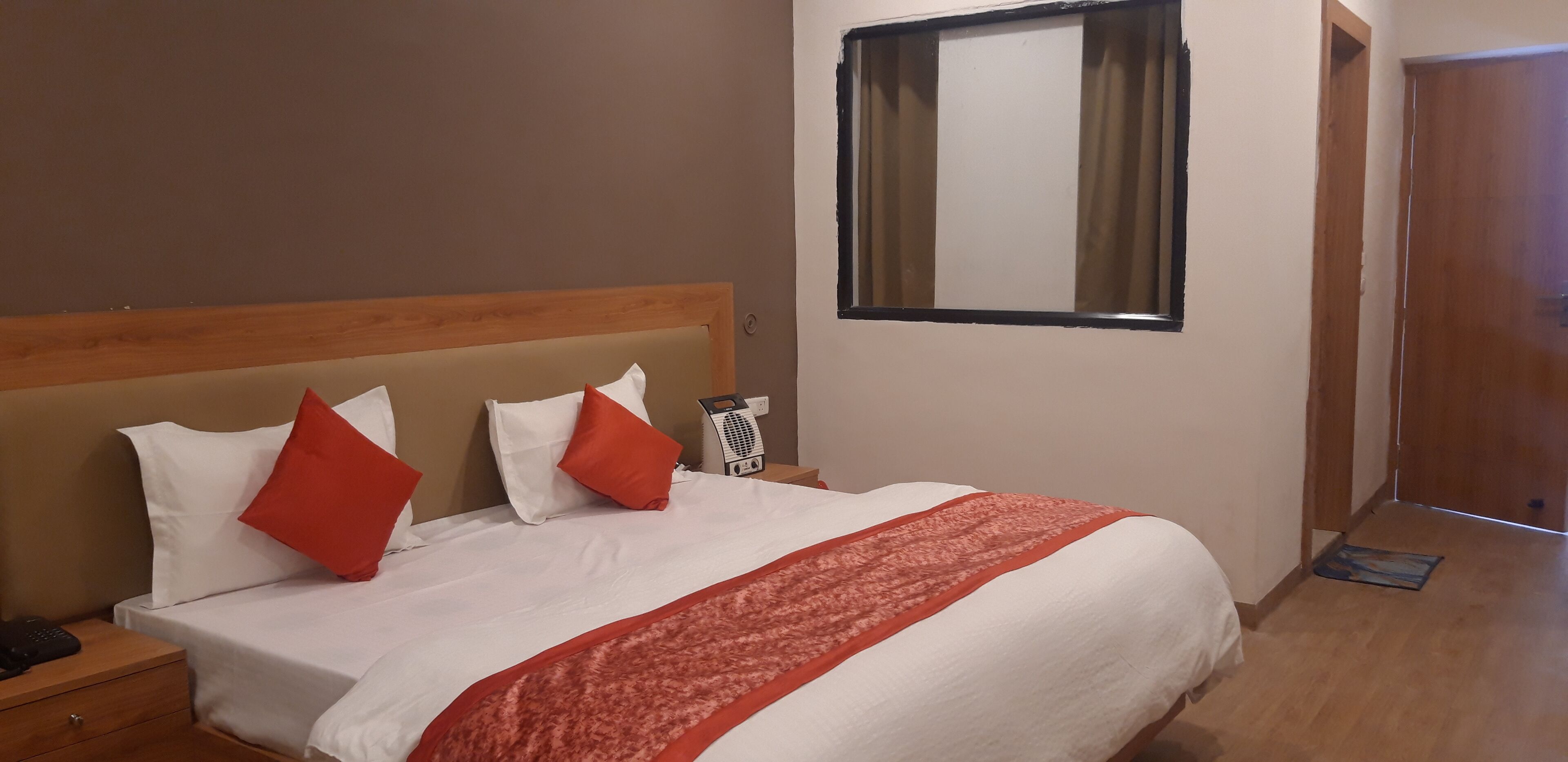A hotel room with a bed, a nightstand, a bedside table, a window, and a door.