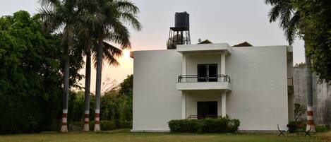 Un edificio moderno con un depósito de agua en el techo, rodeado de palmeras y un área verde.