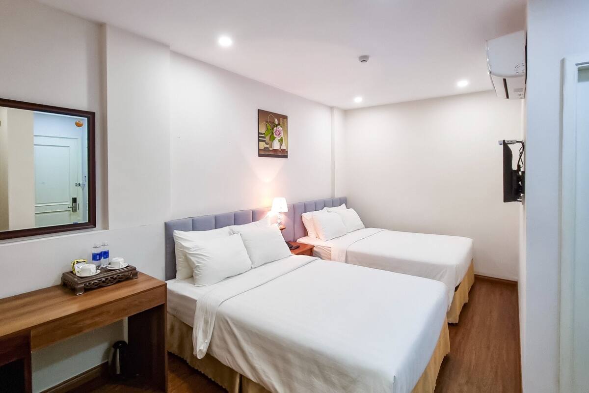 Ein Hotelzimmer mit zwei Betten, einem Schreibtisch, einem Spiegel, einem Gemälde und einem Fernseher.