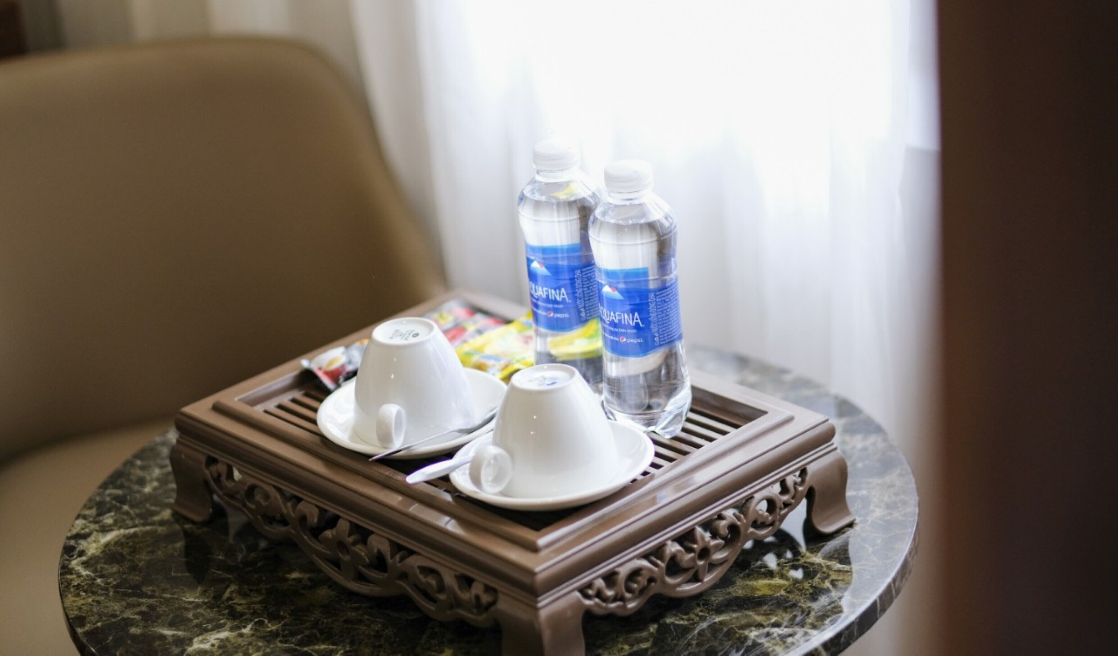 A tray with two white cups and two water bottles on a marble table.