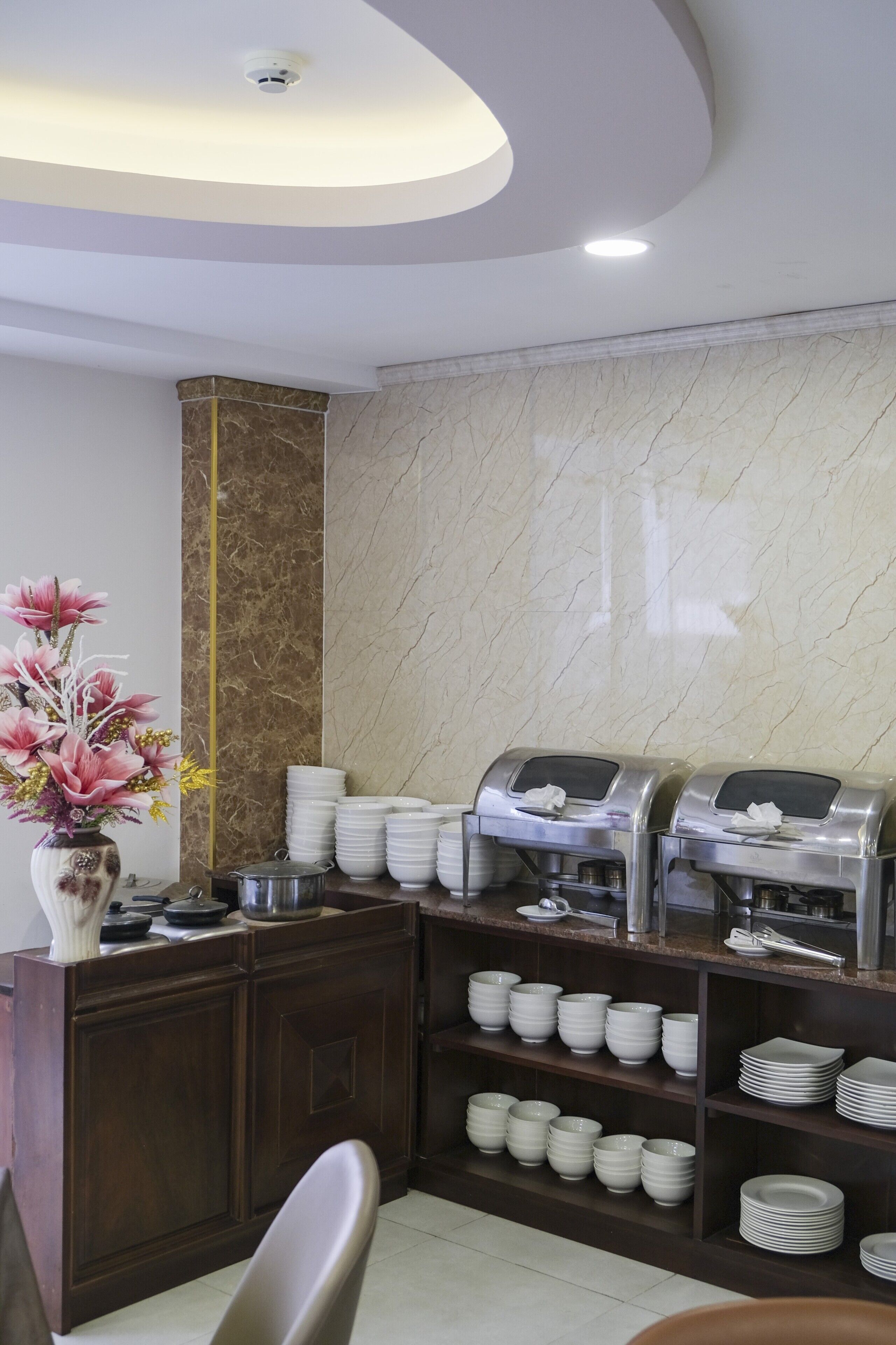 Un espace buffet aux murs de marbre, agrémenté d’un vase de fleurs et où les assiettes et les bols sont soigneusement empilés.