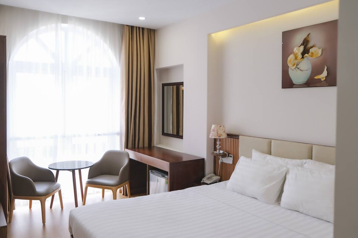 Ein Hotelzimmer mit einem Bett, zwei Stühlen, einem Schreibtisch, einer Lampe und einem Gemälde an der Wand.