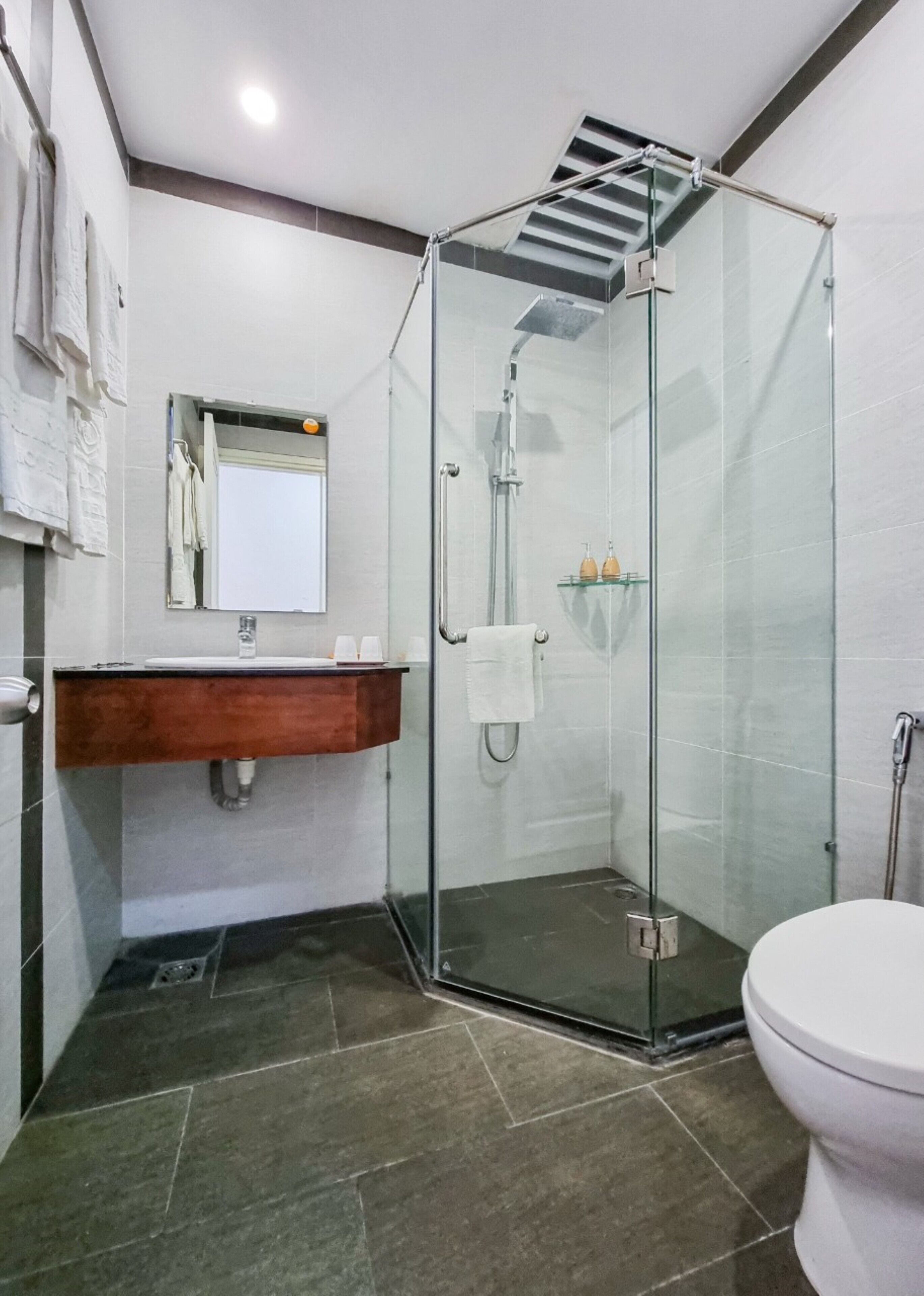 Un baño moderno con cabina de ducha de vidrio, tocador de madera y un inodoro blanco.