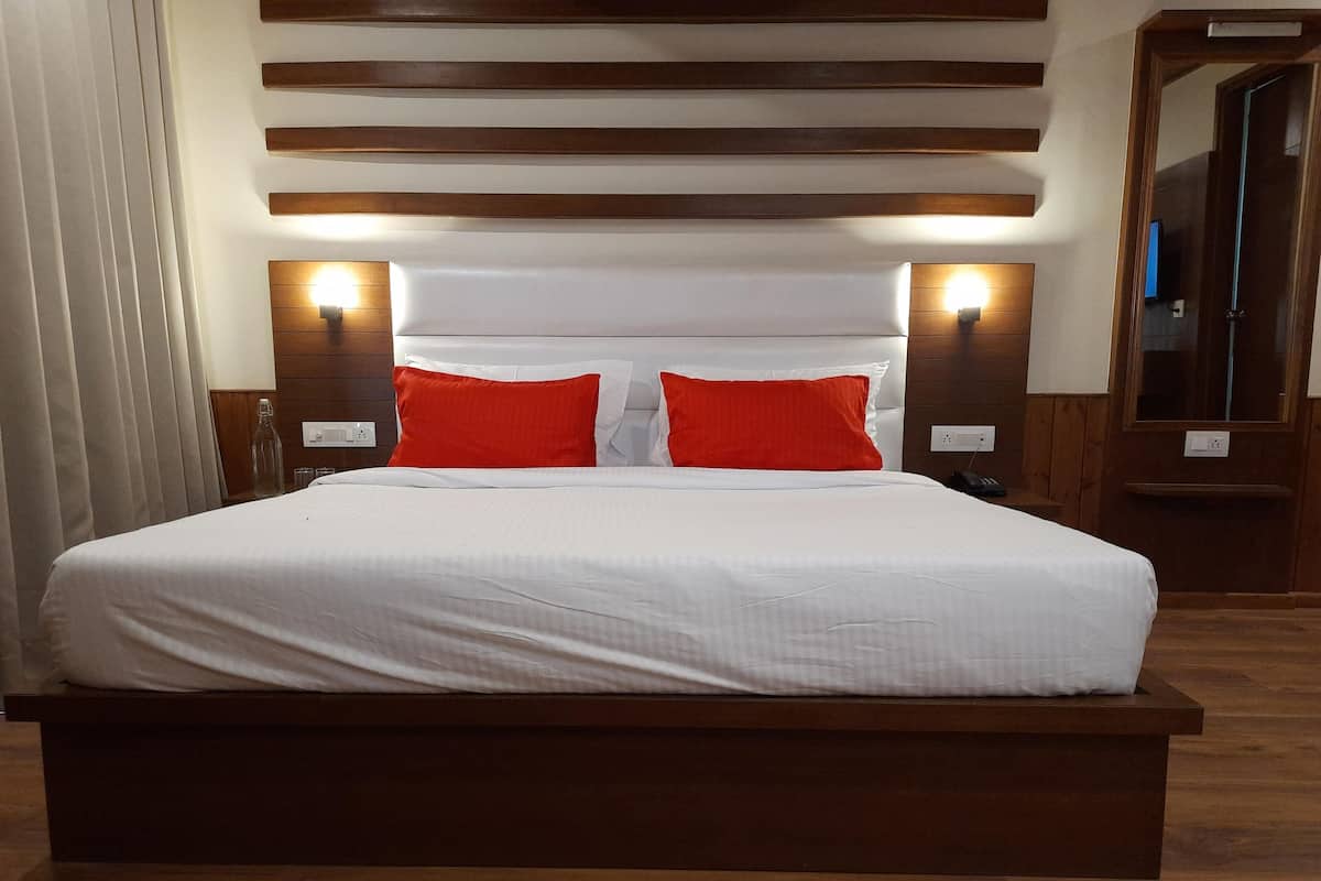 A large bed with white bedding and two red pillows, wooden headboard, and wall-mounted lights.