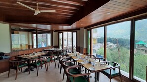 Un comedor con varias mesas y sillas, ventanas amplias que ofrecen vistas al exterior y un ventilador de techo.