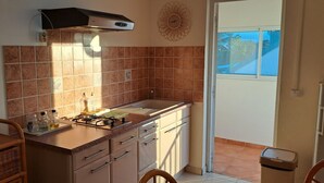 Una cocina compacta con estufa a gas, un lavamanos y ventana con vista a un balcón.