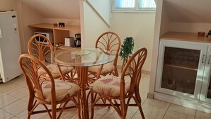 Una cocina compacta con una mesa redonda de vidrio, sillas de mimbre, un refrigerador blanco, un microondas y un armario con puertas de vidrio.