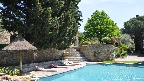 A swimming pool with lounge chairs, stone walls, and a thatched umbrella.