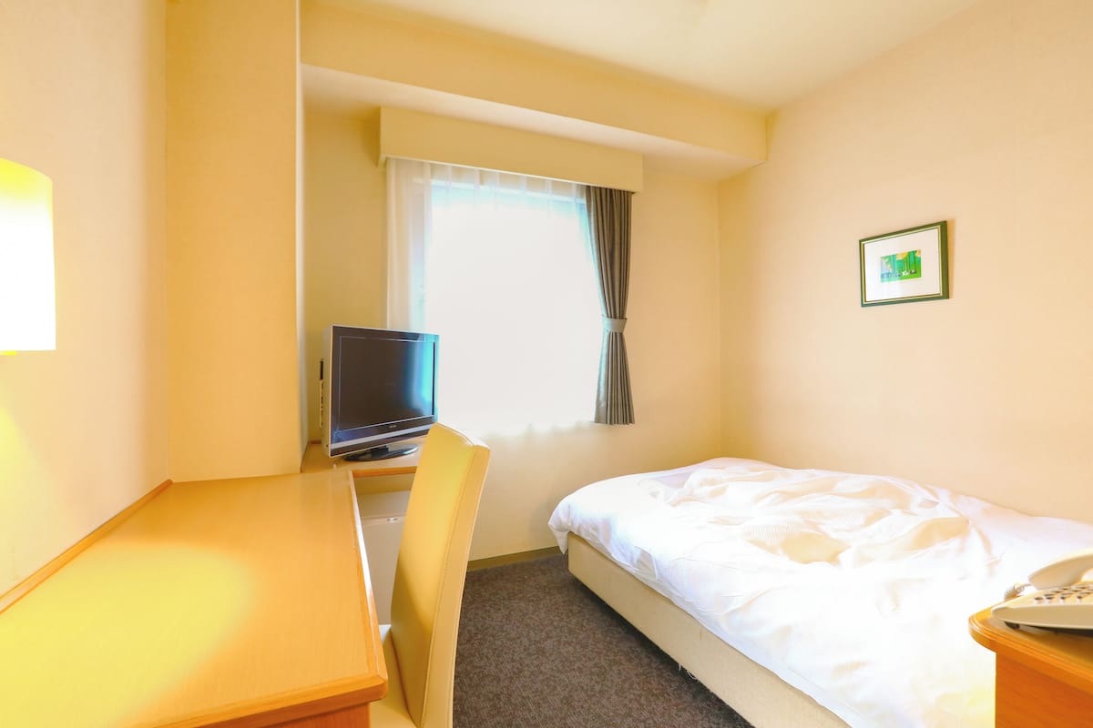 Habitación de hotel con cama, escritorio con computadora, silla, teléfono y ventana con cortinas.