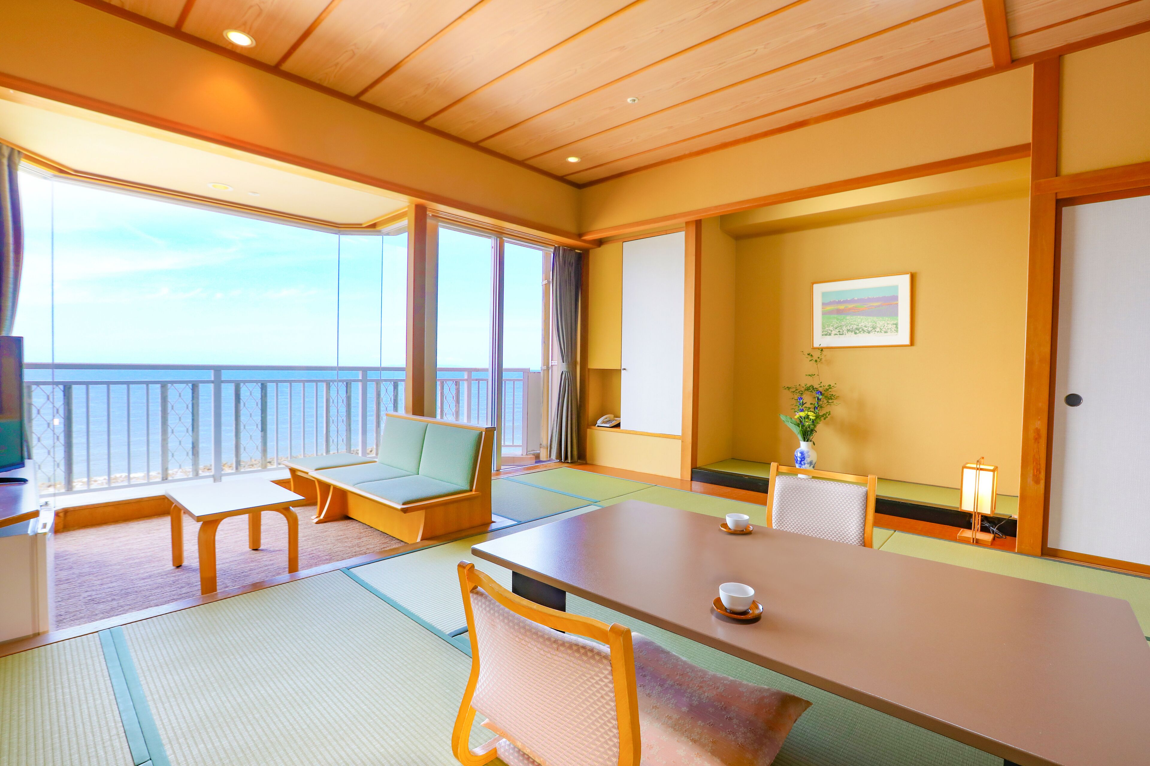 A traditional Japanese room with tatami flooring, a low table, cushioned seating, and a view of the sea.