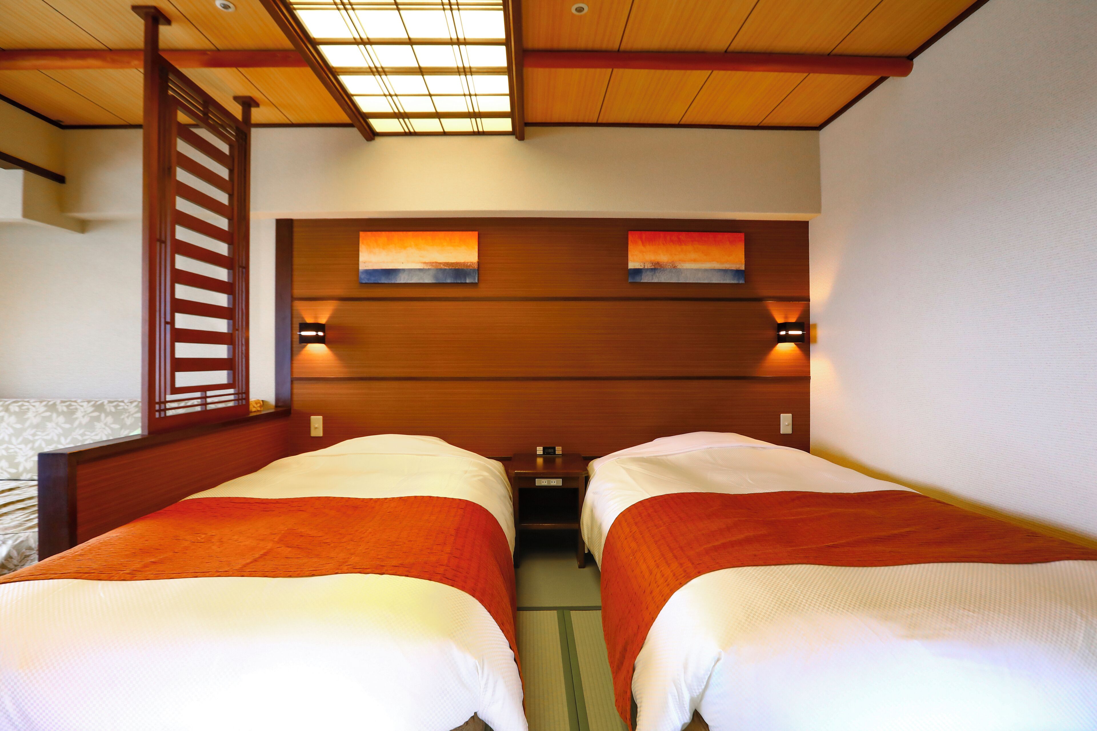 Habitación de hotel con dos camas, cabecero de madera, obra de arte en la pared y una mesita entre las camas.
