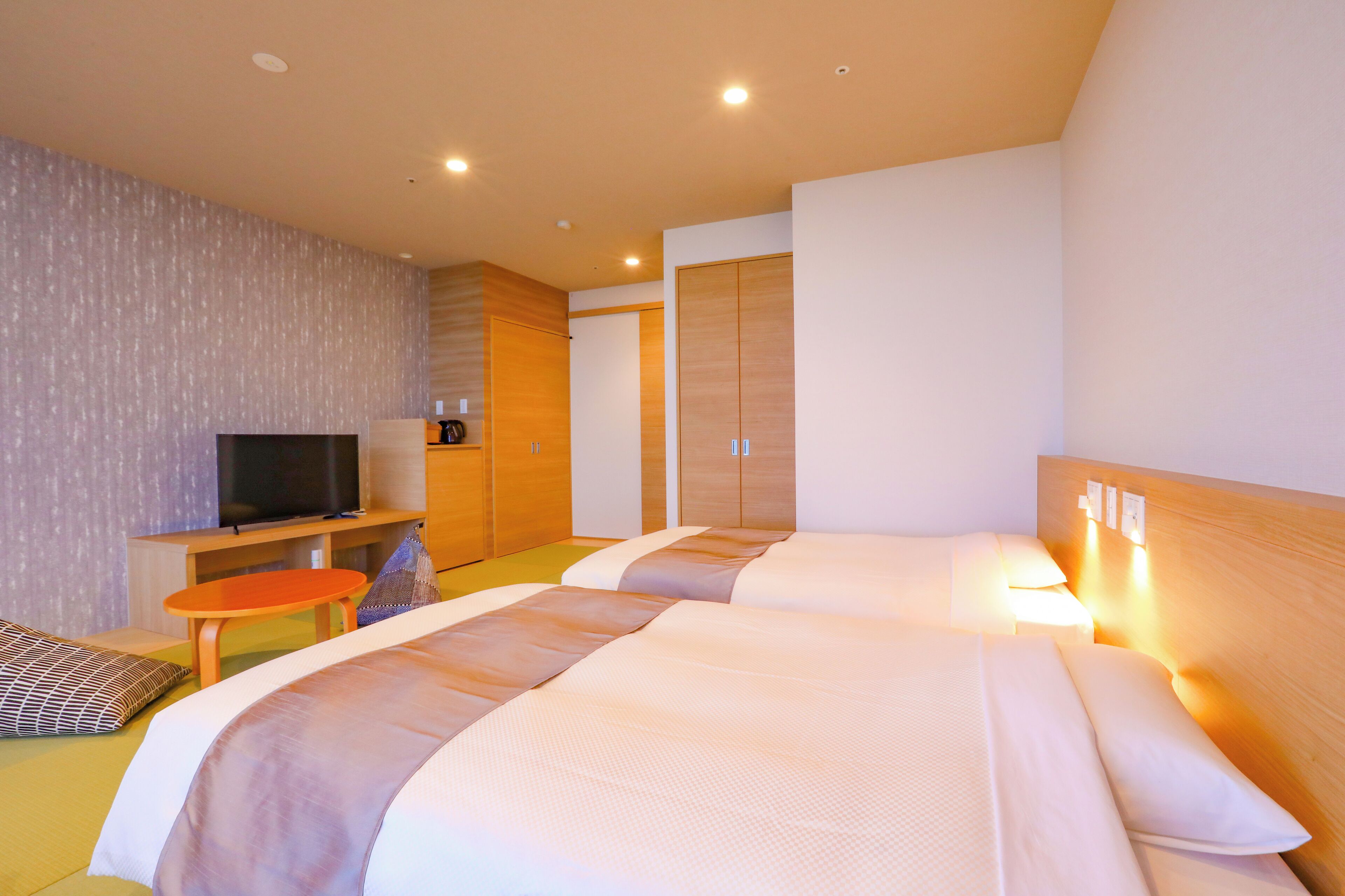 A hotel room with two beds, a television, a small table, and a wardrobe.