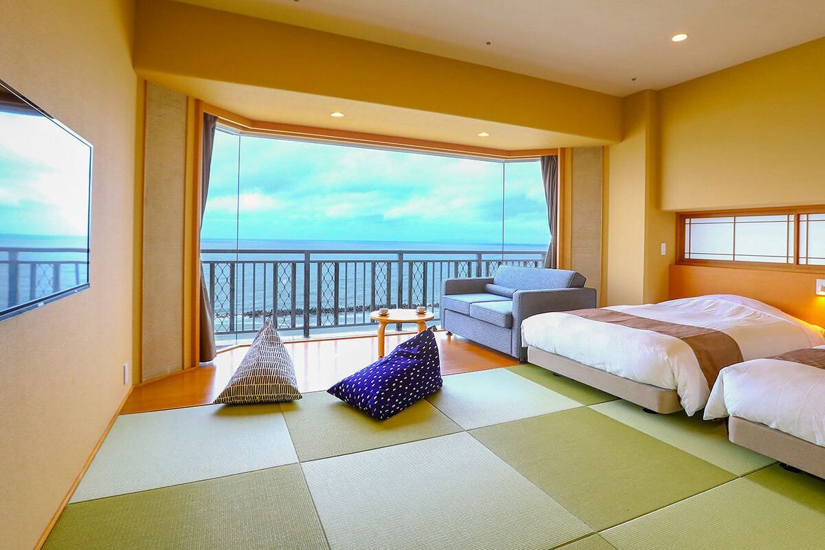 Habitación de hotel con un ventanal grande, un sofá, dos camas y una mesita.