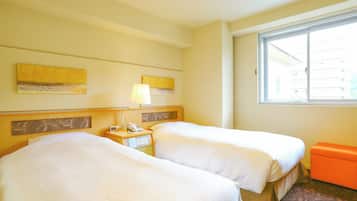 A hotel room with two beds, a nightstand with a lamp, a telephone, and a window with a view of buildings.