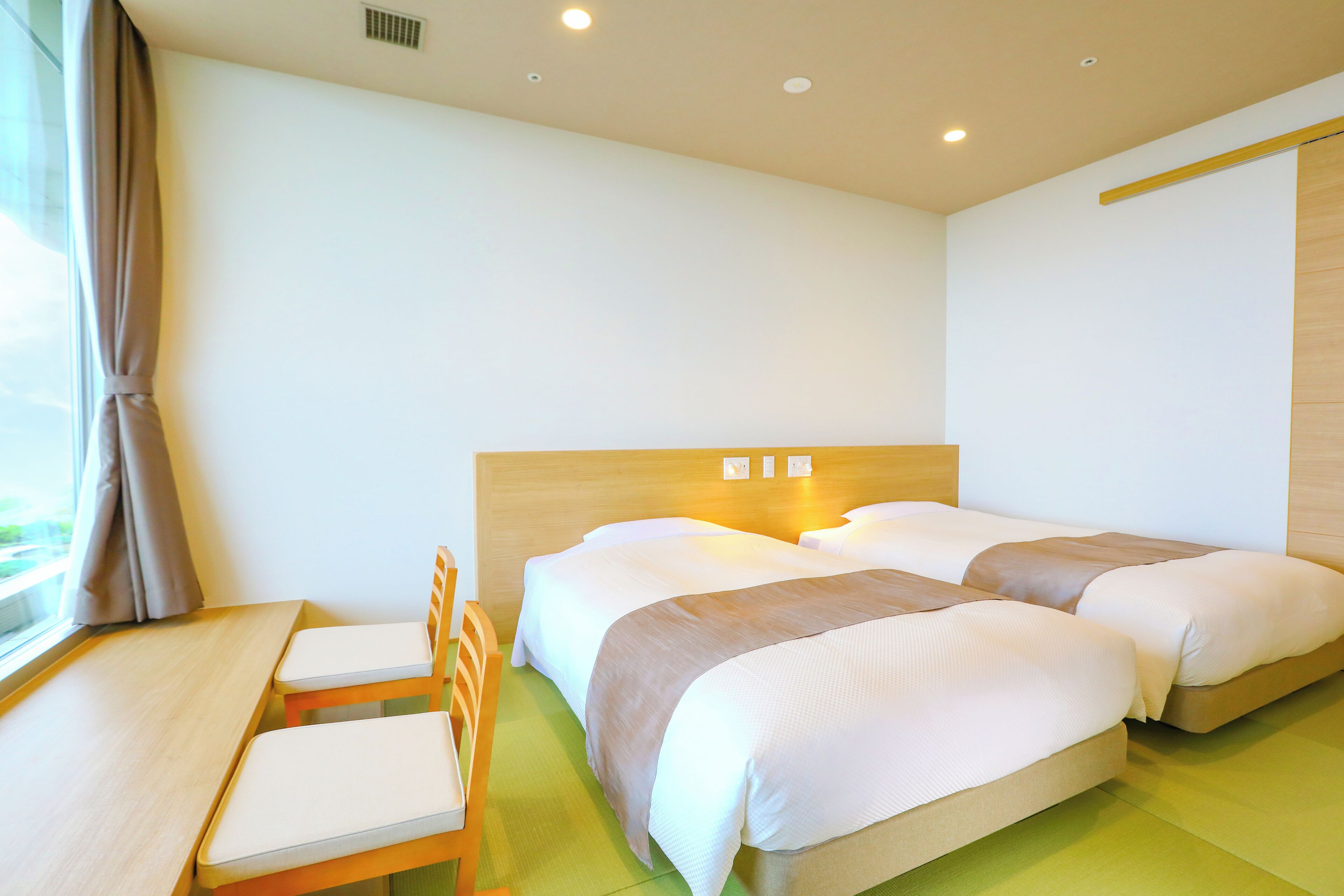 A hotel room with two beds, a wooden desk, and a chair.