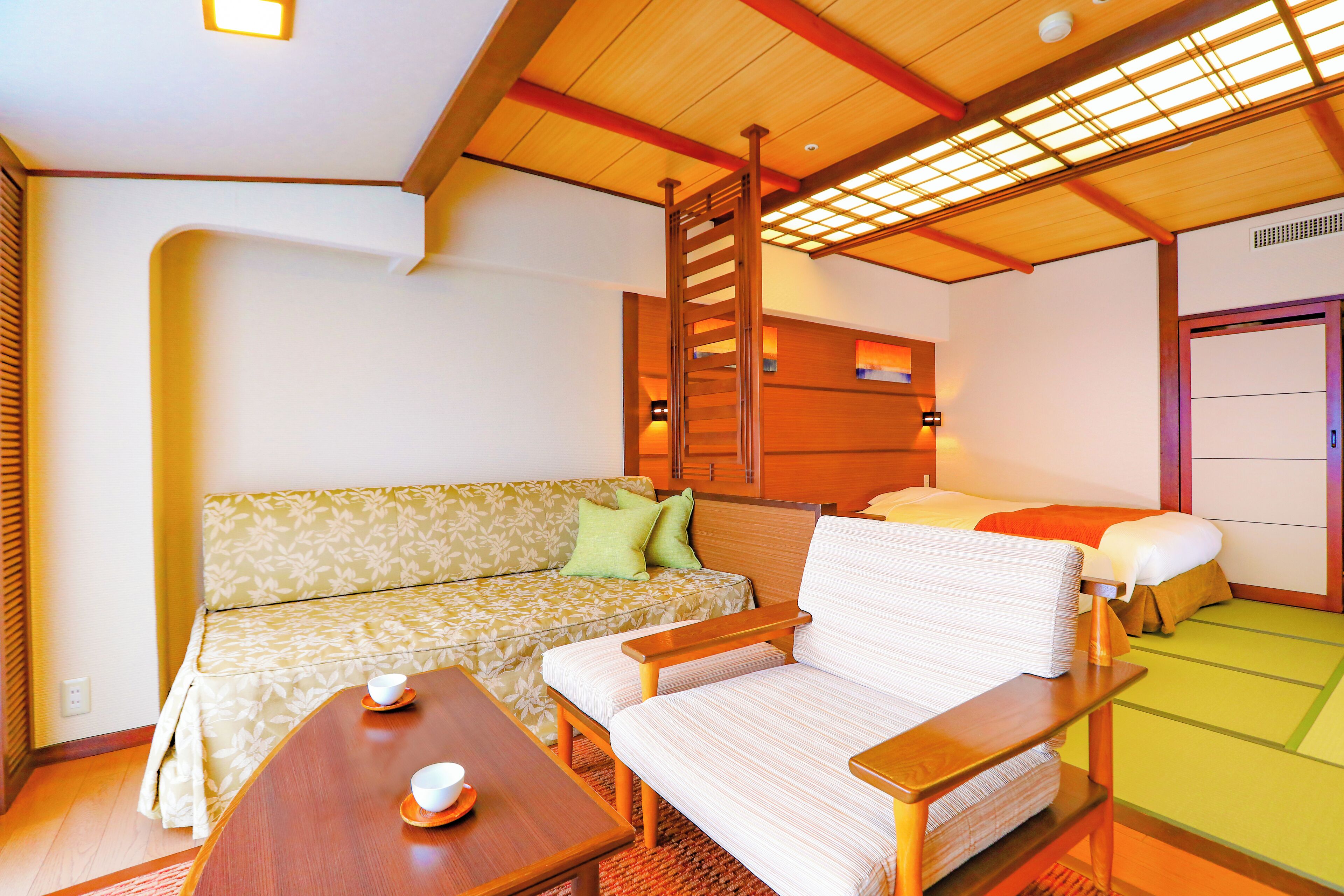 A traditional Japanese-style room with tatami flooring, a low wooden table, a sofa, and a bed with a wooden headboard.