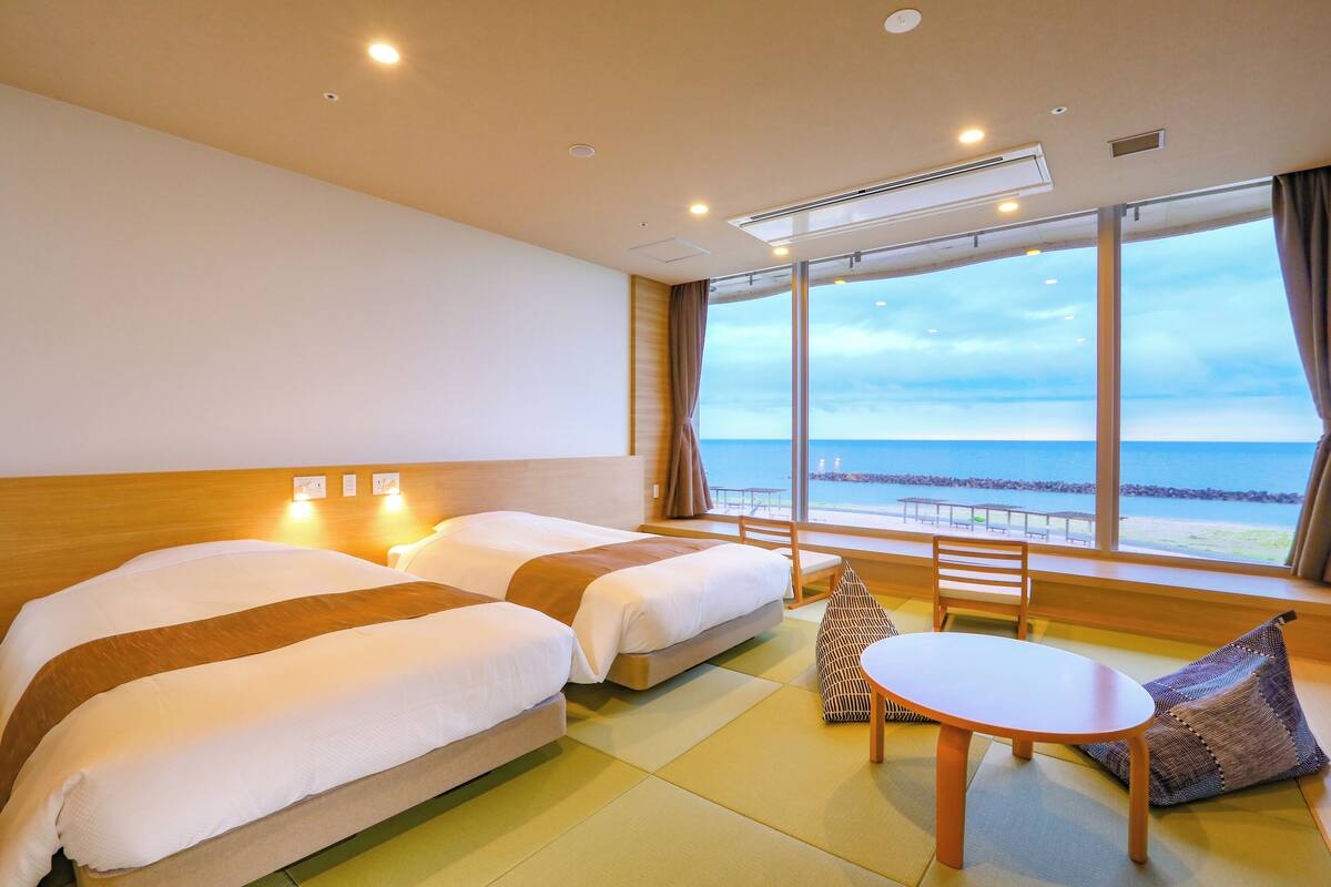 Habitación de hotel con dos camas, una mesita y vista al mar.